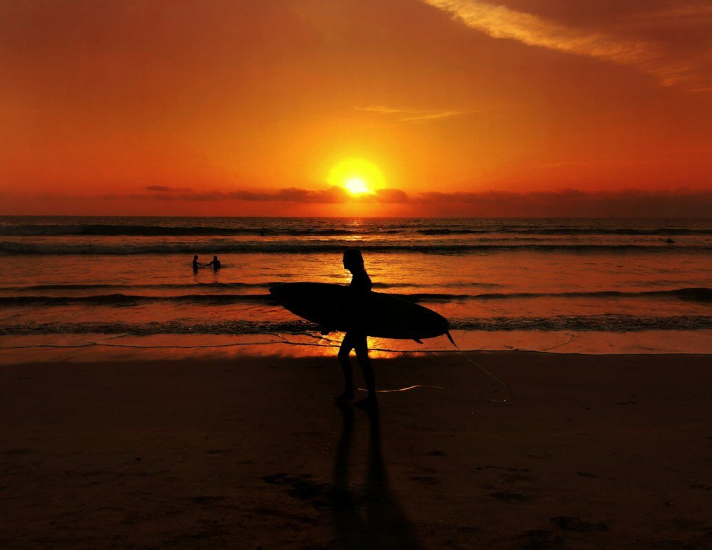 Silhouette eines Surfers mit Surfbrett beim Spaziergang am Strand bei goldenem Sonnenuntergang