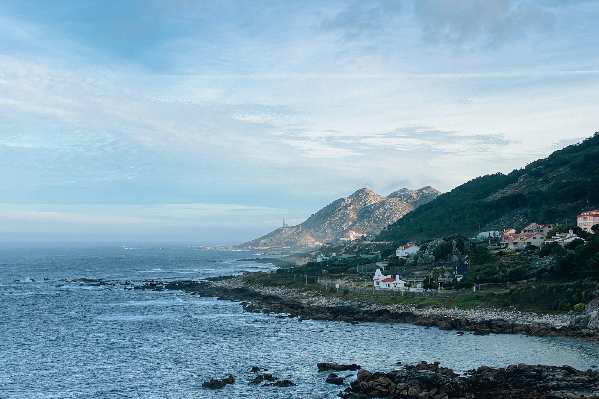 A calm inlet with homes climbing a green Galician hillside