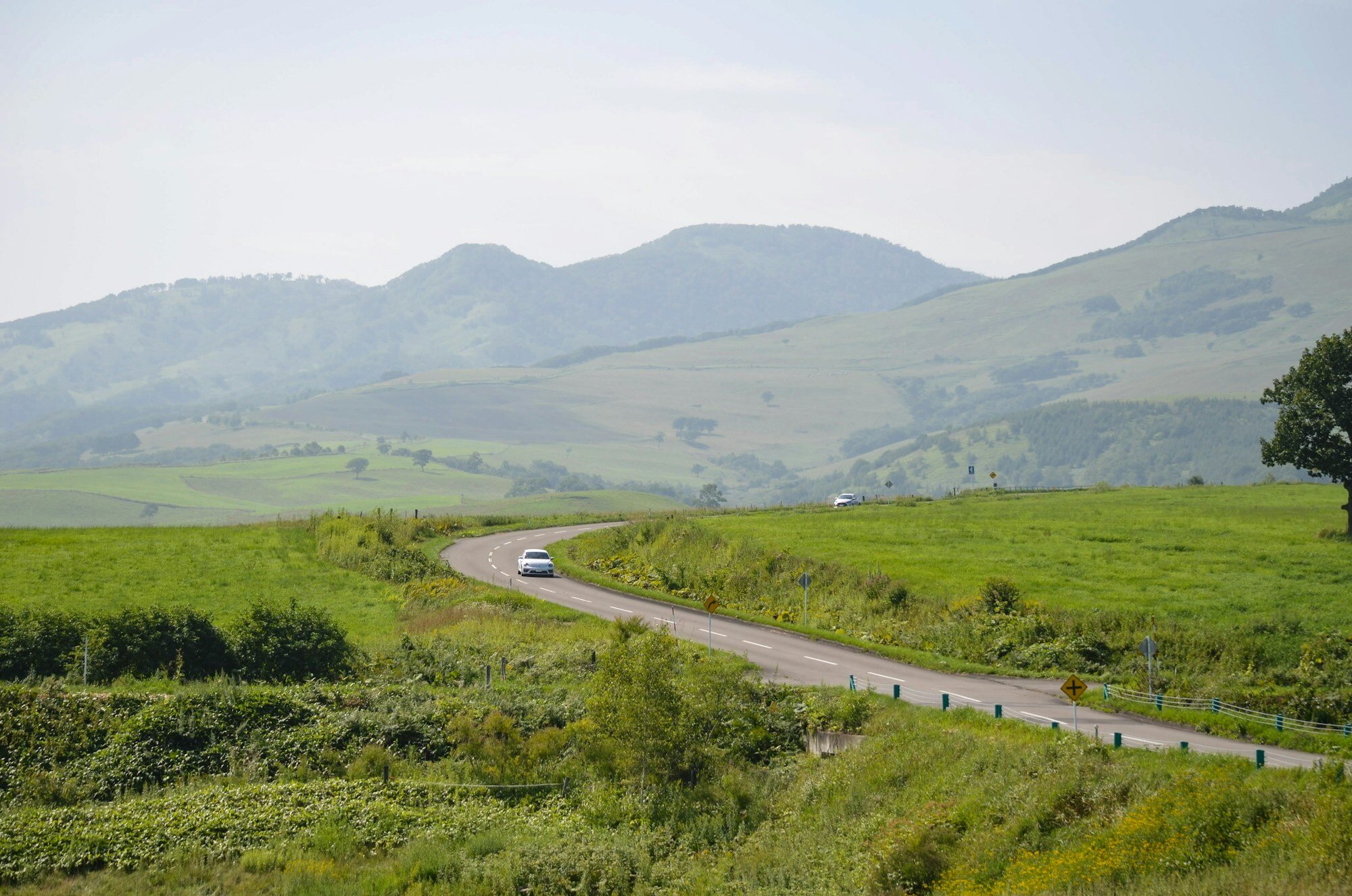 Car driving along scenic mountain road through Hokkaido pastoral landscape