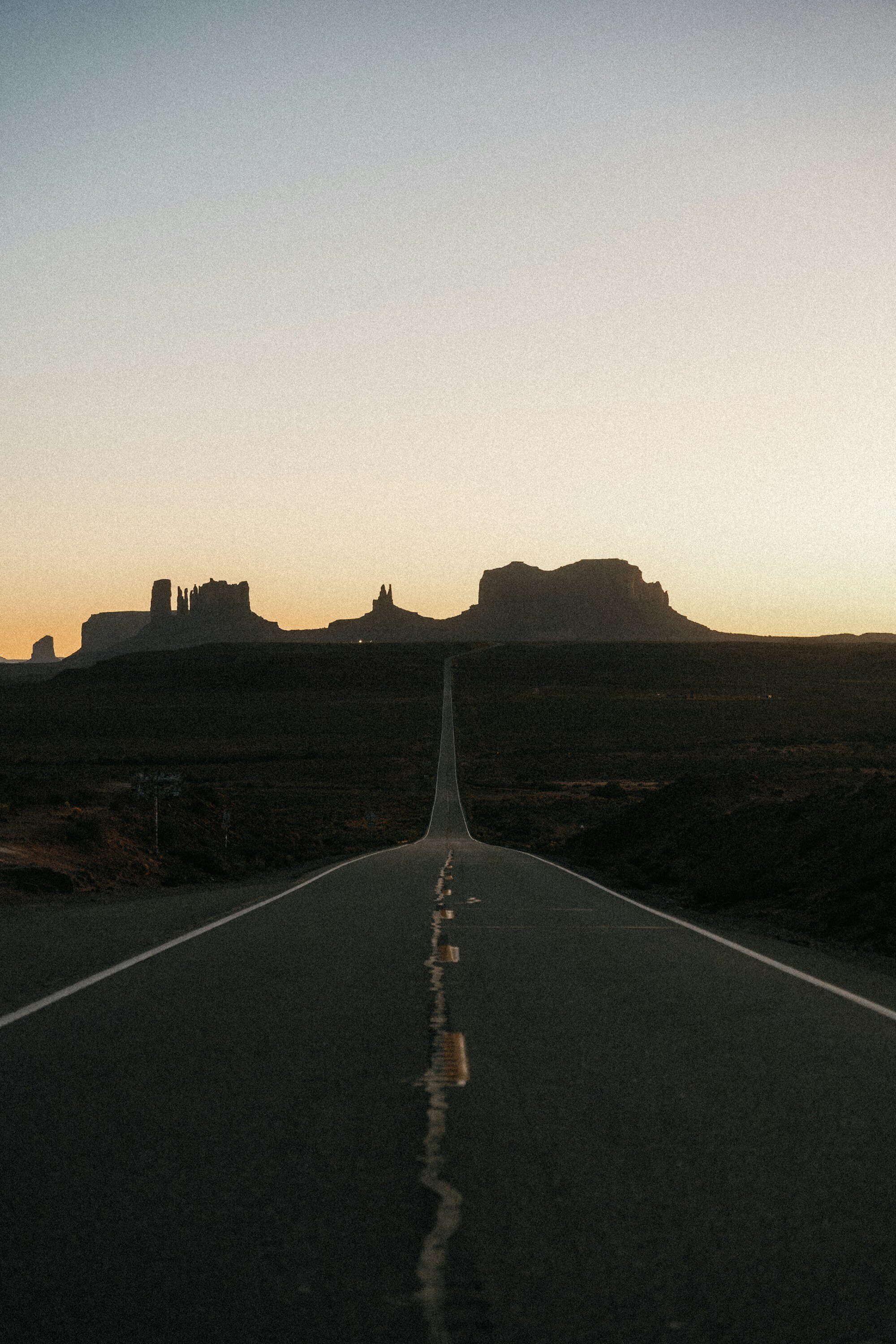 Carretera desértica durante la hora dorada con las mesetas de Monument Valley: paisaje del suroeste estadounidense
